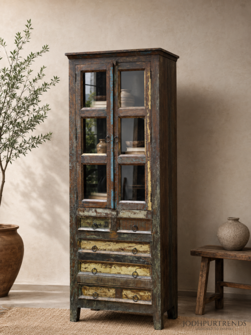 Tall multicolor reclaimed wood display cabinet with glass-paned doors and five drawers in a distressed boho finish, styled with ceramic vases against a beige wall at jodhpurtrends.in